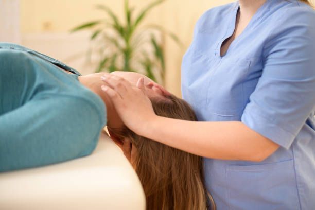 Therapist in scrubs providing neck treatment for person lying on table in wellness clinic care.