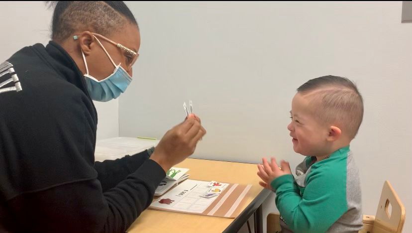 Adult holding a card for a smiling child with Down syndrome at a table.