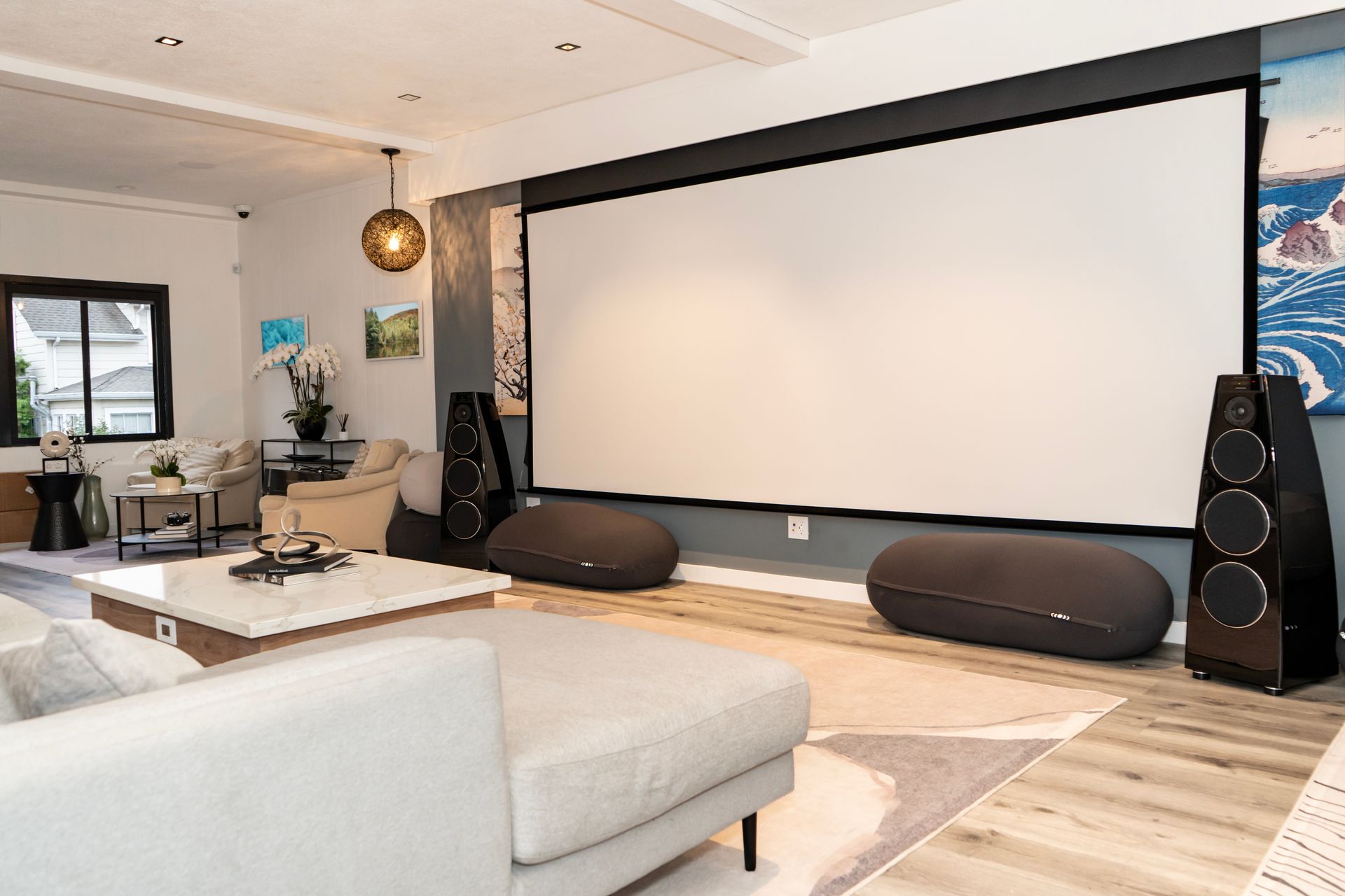 Modern home theater with a large projector screen, black speakers, and a light gray sectional sofa.