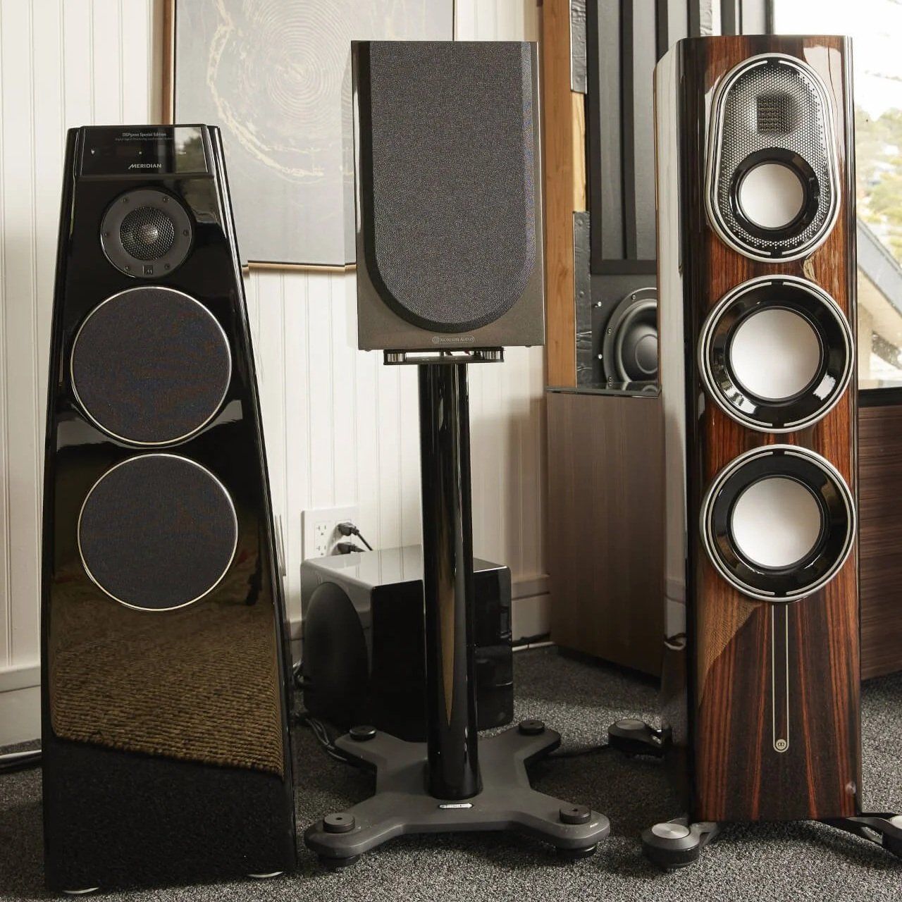 Three large floorstanding speakers in a room, including black and wood-grain models