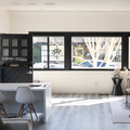 Modern living room with black-framed windows, white table, gray chairs, and sunlit wood floor