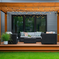 Covered backyard deck with wicker seating, string lights, and potted greenery