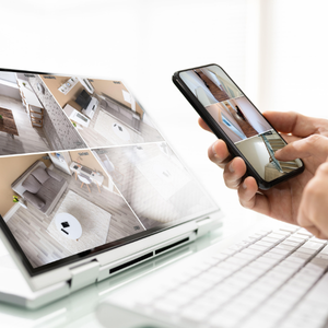 Hand holding a smartphone viewing a live camera feed of a small white laptop on a desk