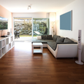 Bright living room with wood floors, gray sectional sofa, TV, and large sliding glass doors to a patio.