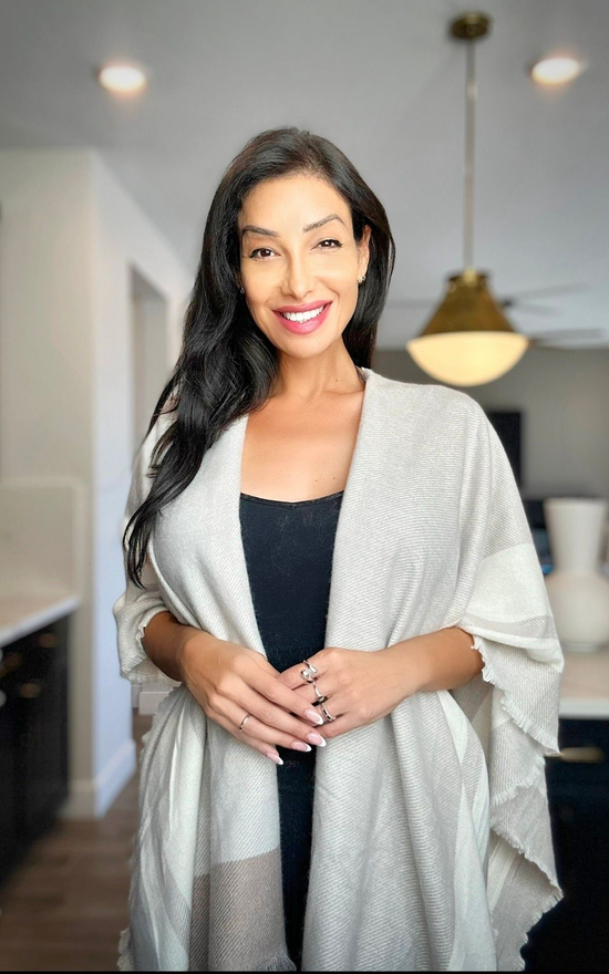 A woman is sitting at a desk with a laptop and a vase of flowers.