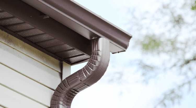 A brown metal gutter and downspout attached to the corner of on a home in Huntsville, AL by LJ Roofing