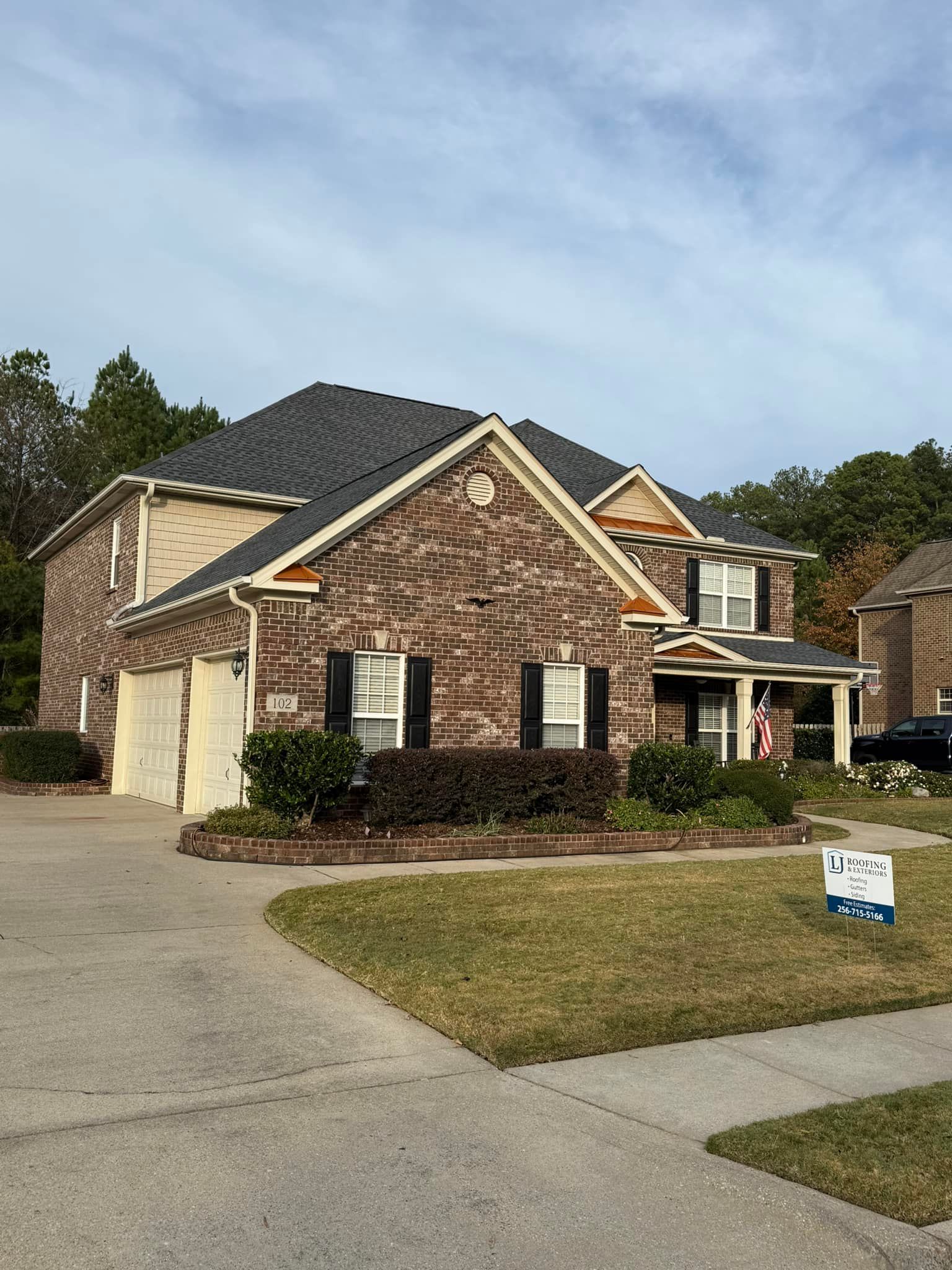 A brick, two-story suburban home with a dark shingled roof in Huntsville AL by LJ Roofing