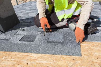 A roof repair in Huntsville AL using a tool to install grey asphalt roofing shingles on a wooden roof deck.