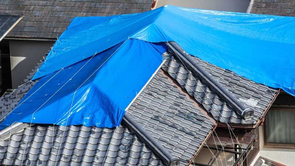 A blue tarp is secured over a section of a tiled roof to provide temporary protection in Huntsville AL by LJ Roofing