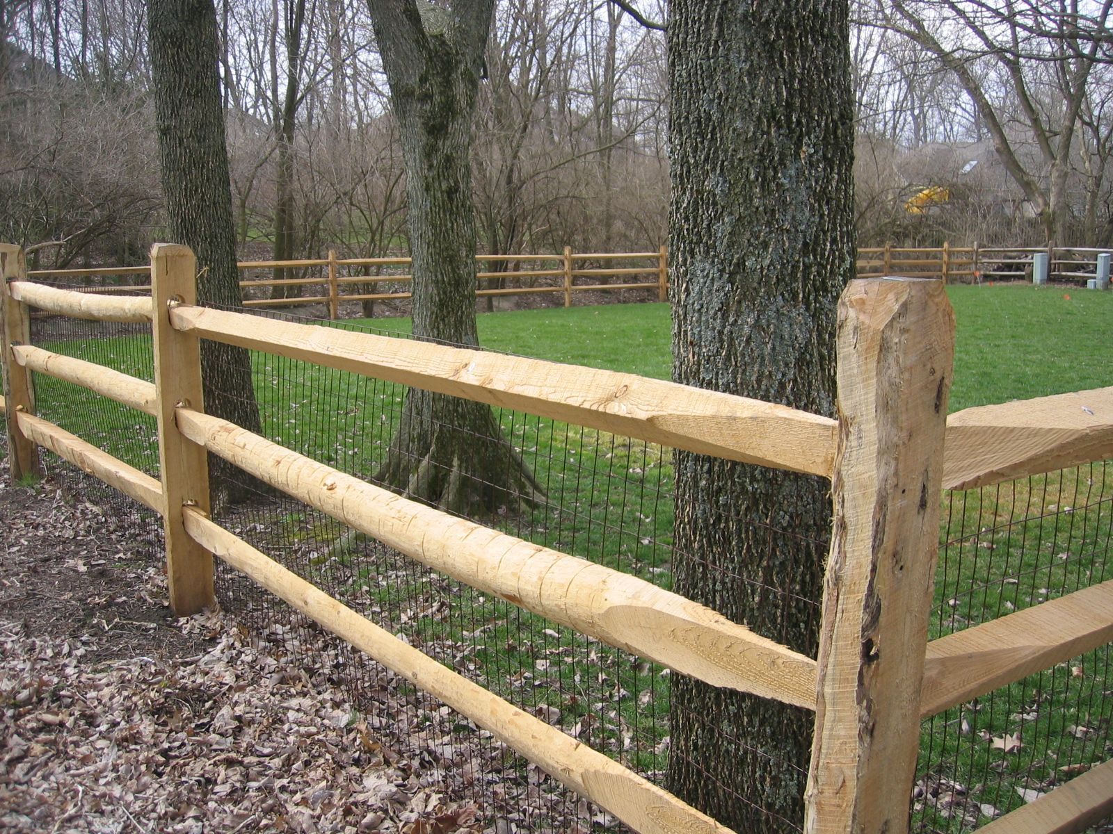 a wooden fence surrounds a grassy field with trees in the background