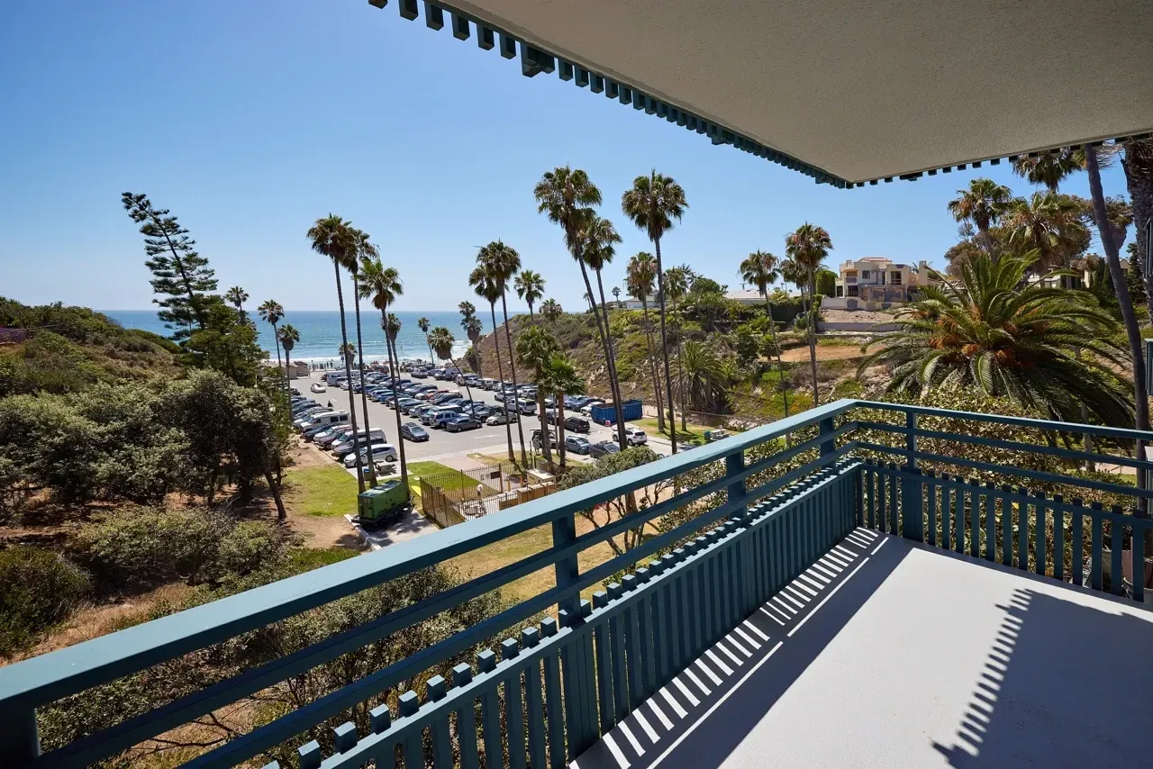 View from a balcony overlooking a beach parking lot, palm trees, and the ocean.