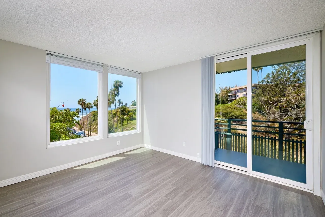 Living room with large windows and a sliding glass door offering ocean and greenery views.