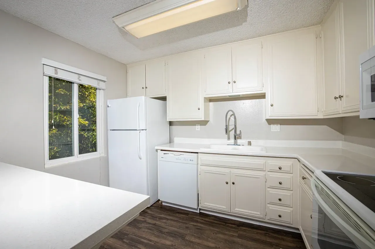Kitchen with white cabinets, countertops, and appliances, including a refrigerator, dishwasher, and oven.