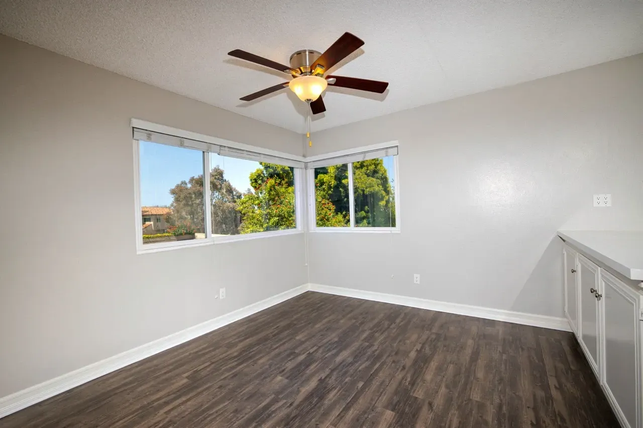 Empty room with large windows, a ceiling fan, and built-in cabinets.