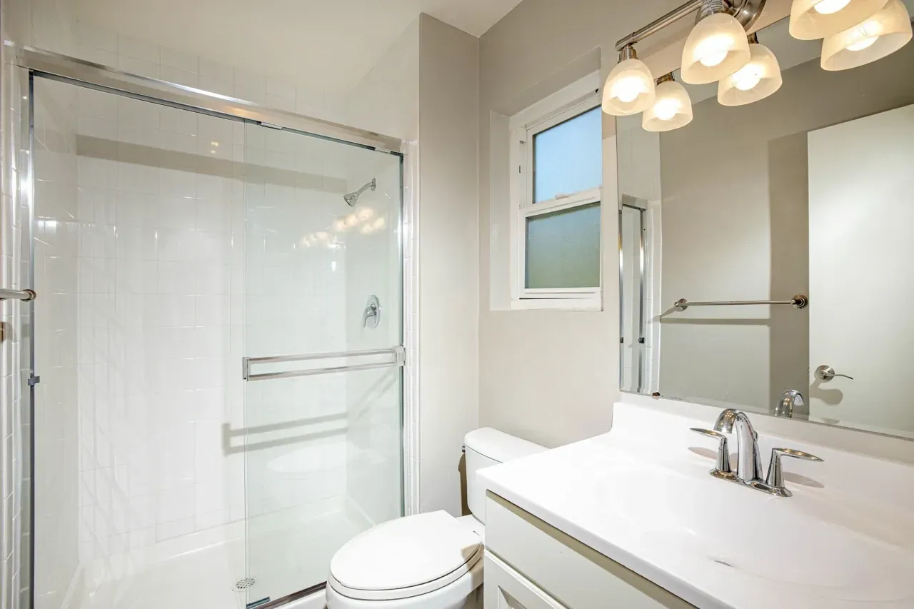 Modern bathroom with white tiled shower, toilet, and vanity with chrome fixtures.