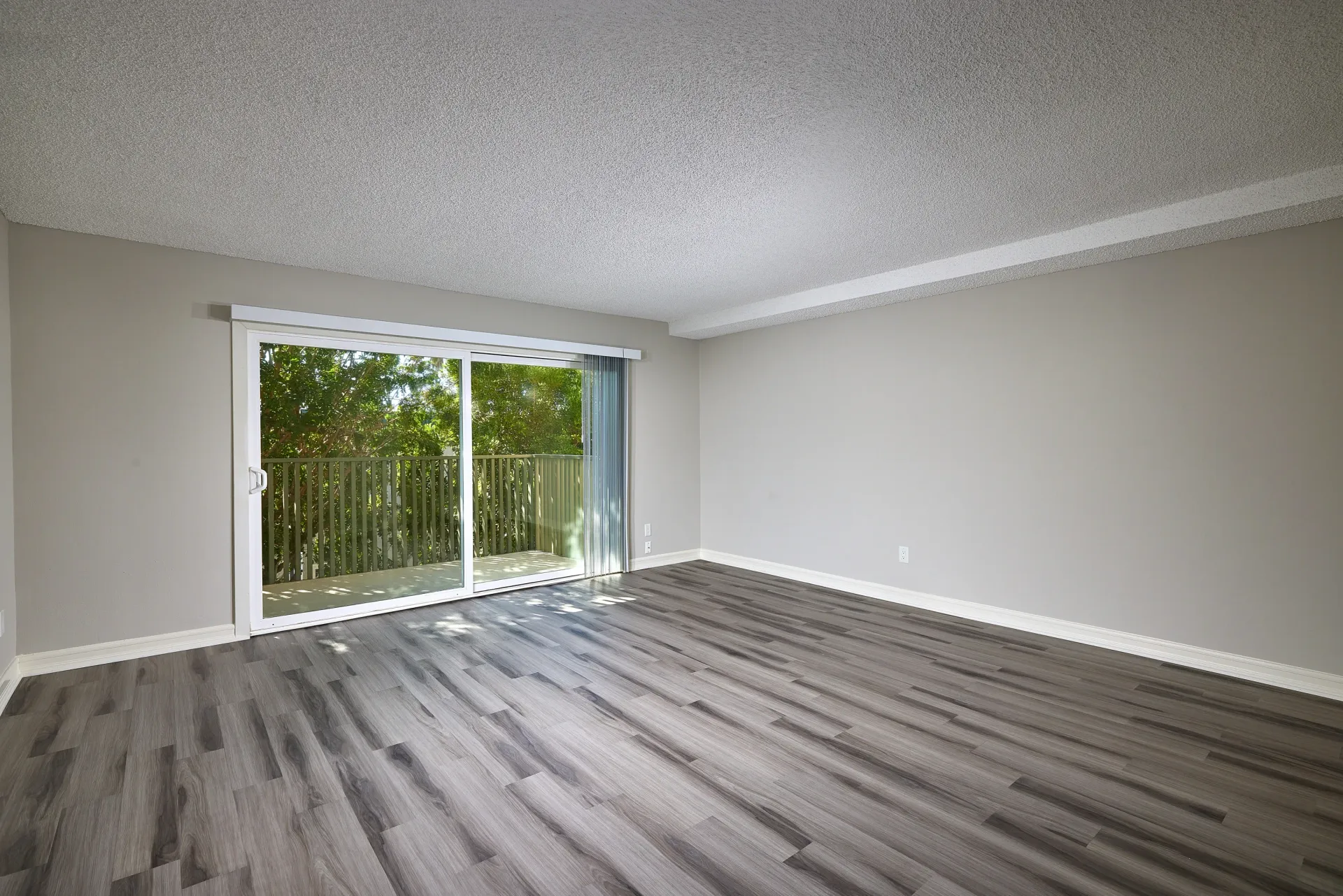 Empty apartment living room with sliding glass door to balcony and wood-look flooring