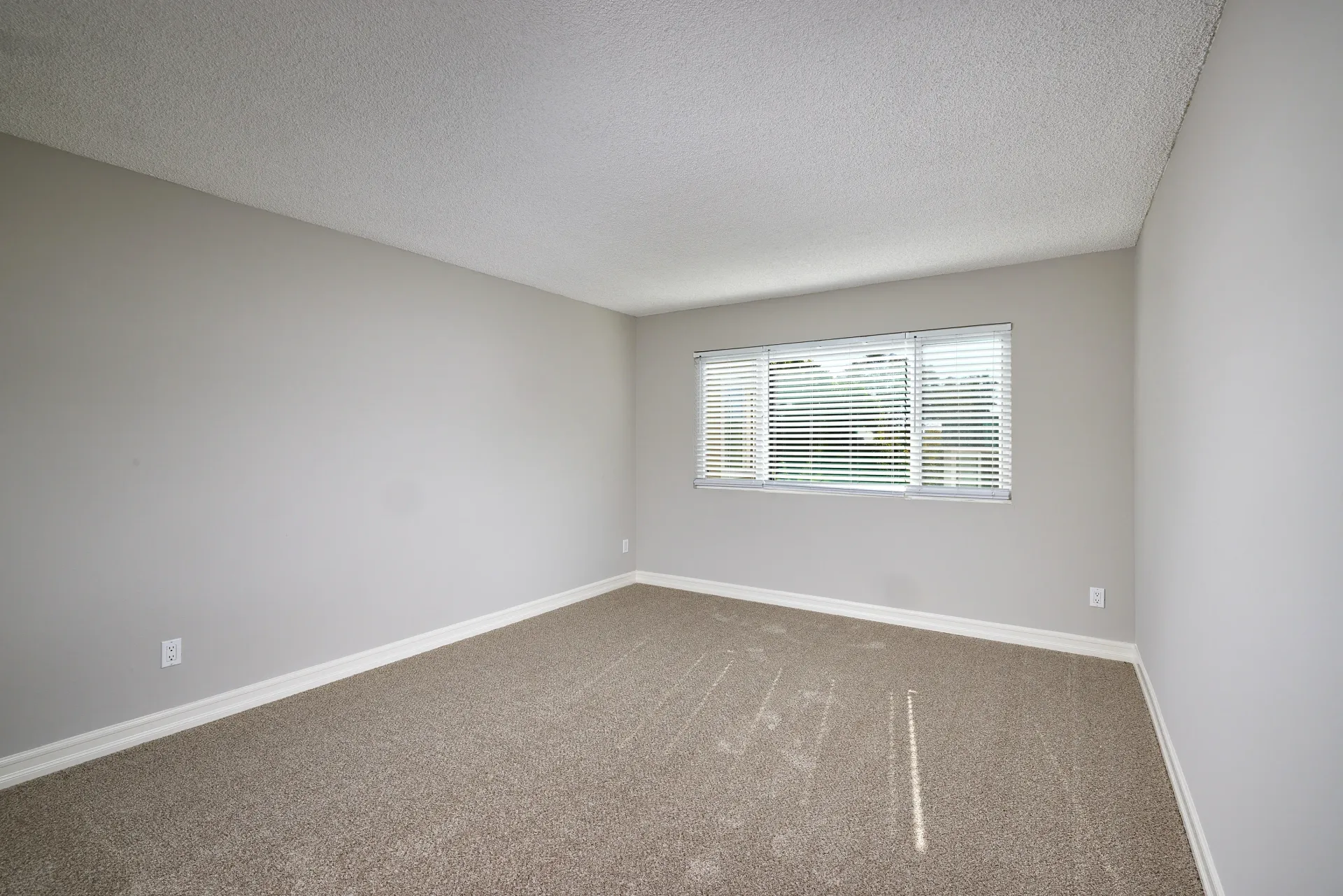Empty bedroom with neutral carpet and a large window with blinds.