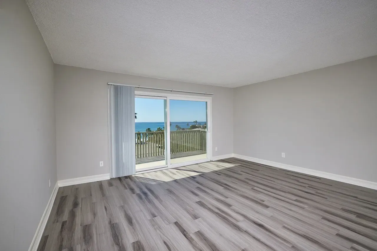 Empty living room with sliding glass door leading to a balcony with ocean view.