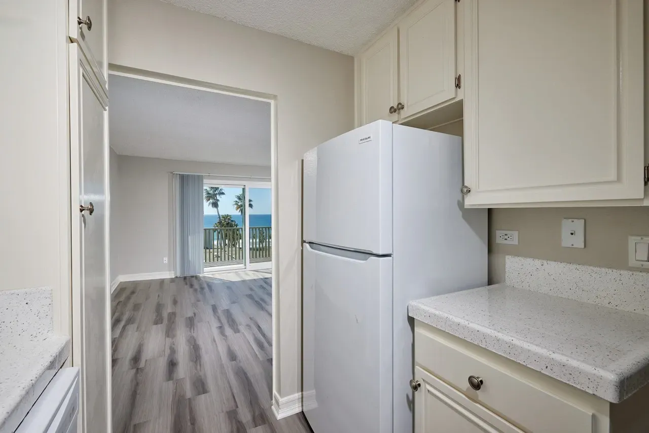 Kitchen view showing a refrigerator and cabinets, with a doorway leading to a living area and ocean view.