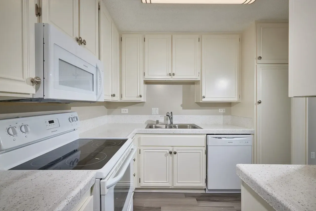 Kitchen with white cabinets, granite countertops, stainless steel sink, white microwave, and stove.