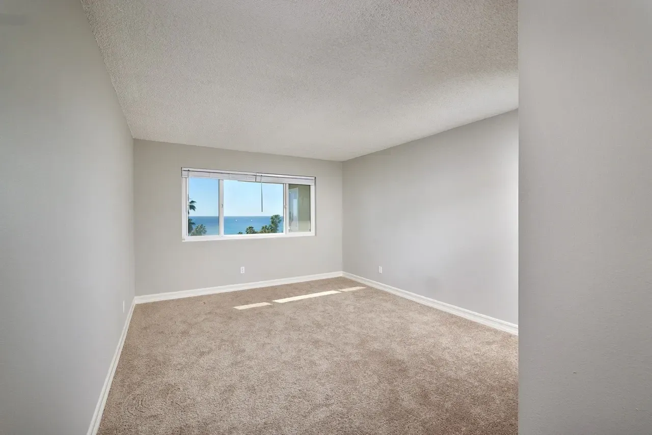 Empty bedroom with carpet and a large window showing ocean view.