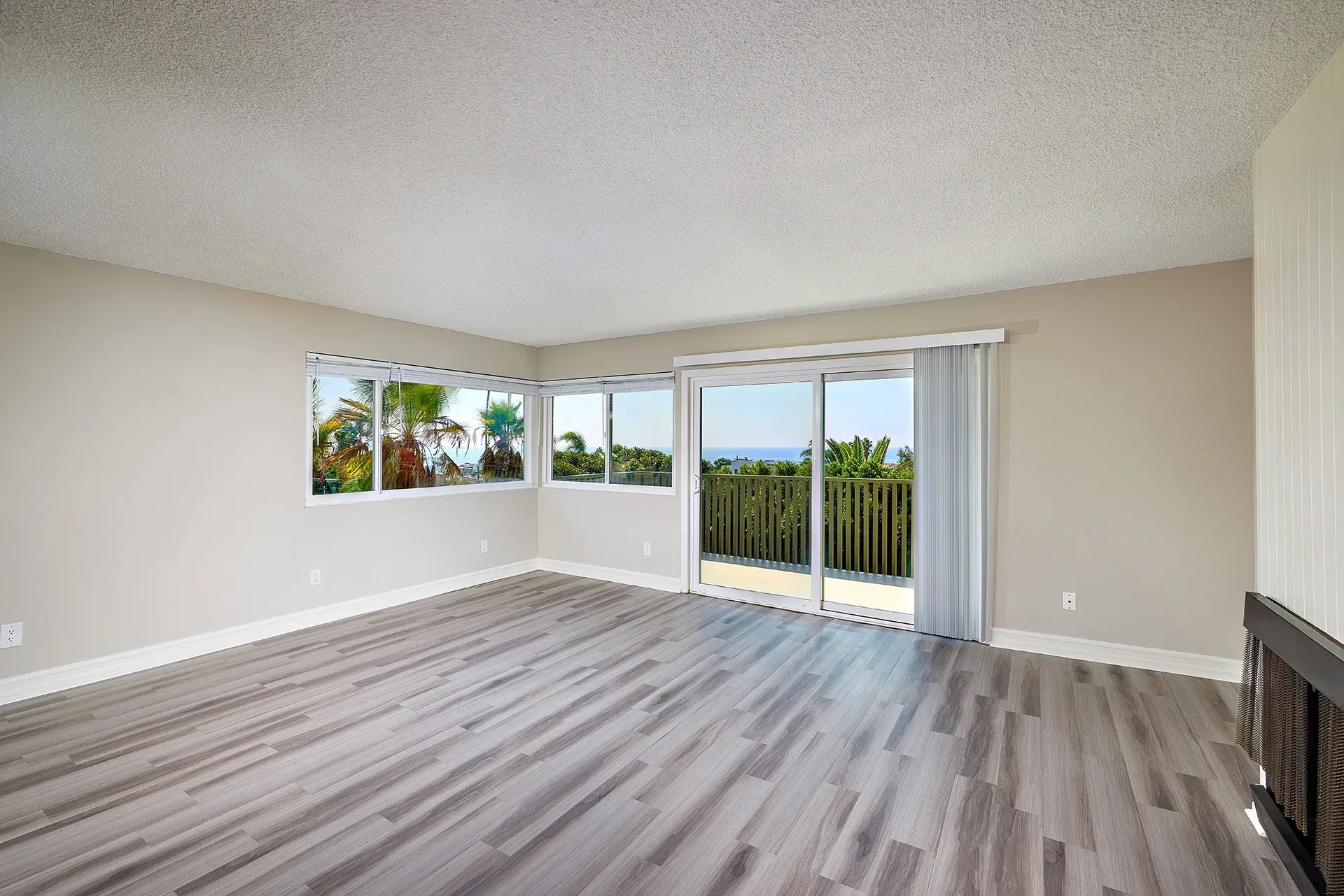 Spacious living room with large windows and a sliding glass door offering ocean and tropical foliage views.