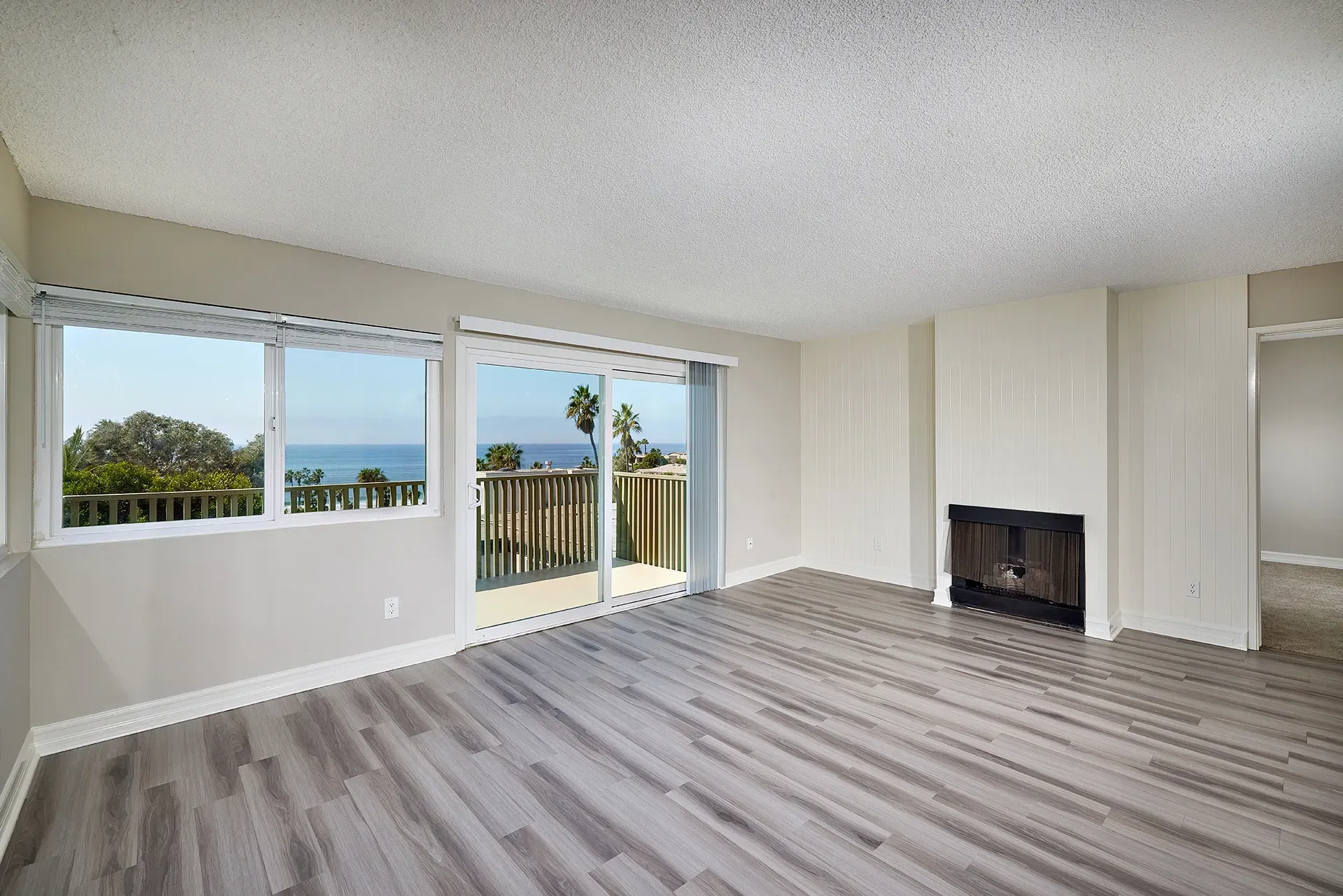 Empty living room with a fireplace and large windows overlooking the ocean and balcony.