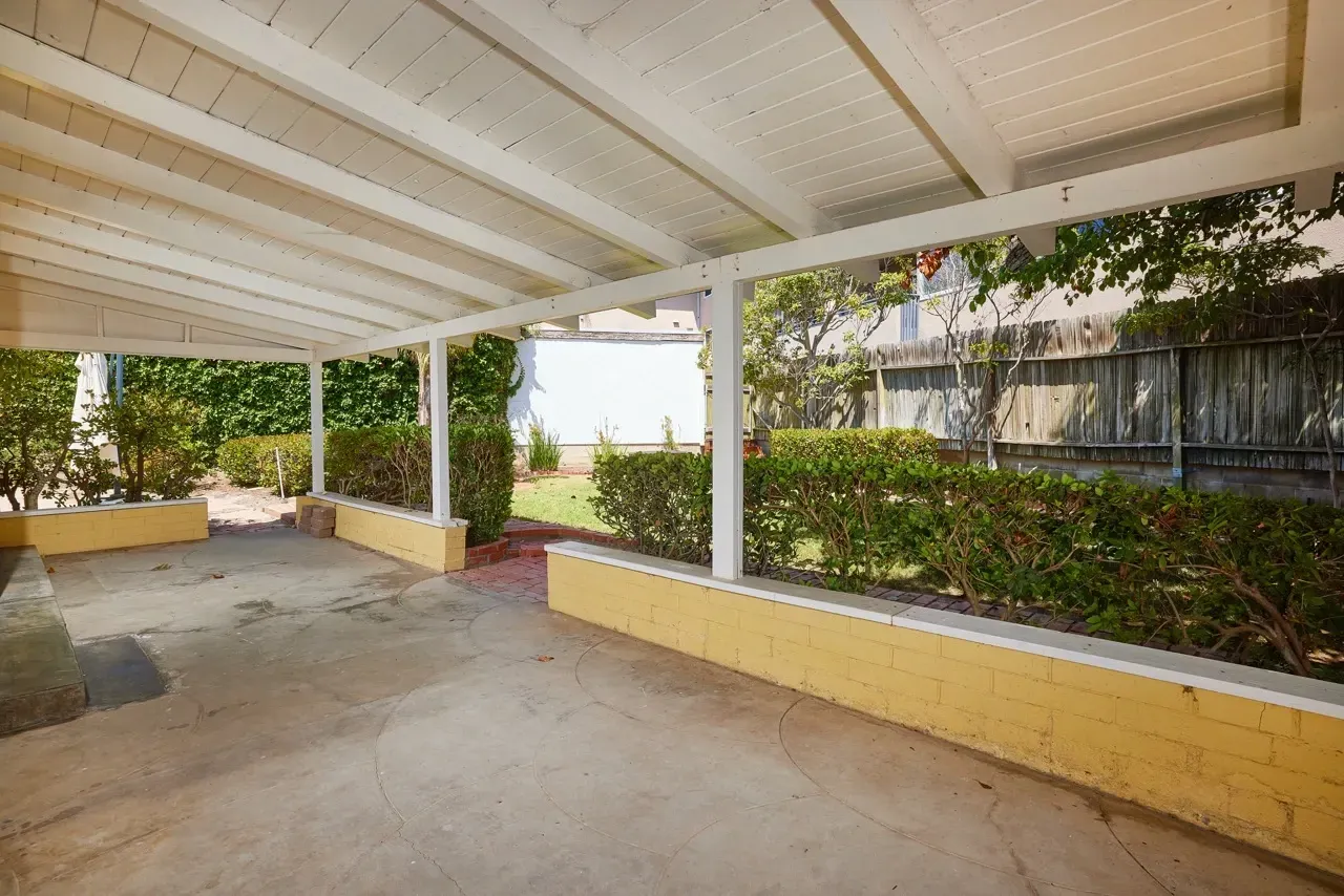 Covered patio with surrounding greenery and a wooden fence.
