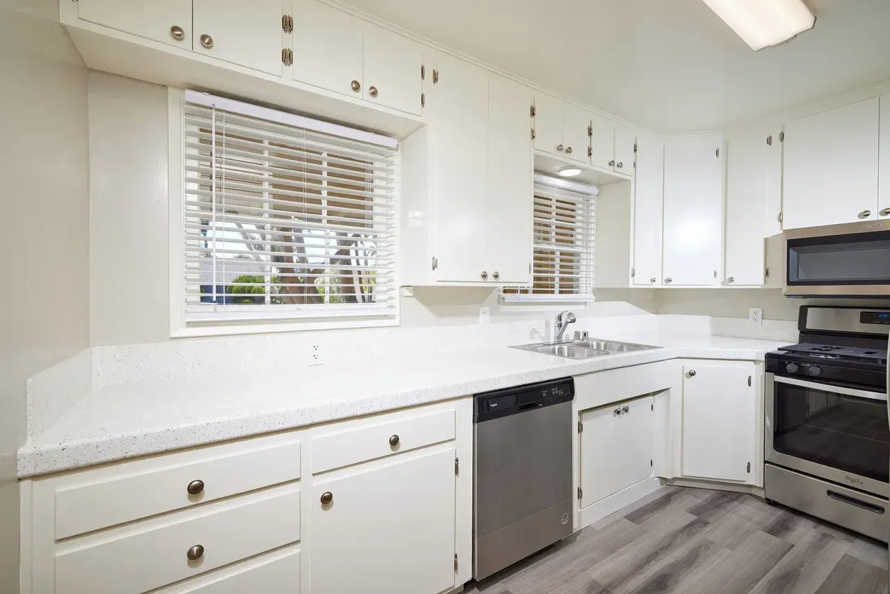 White kitchen with white countertops, stainless steel appliances including a dishwasher, oven, and microwave.