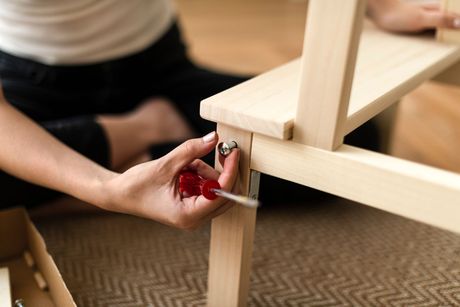 A woman is sitting on the floor assembling a wooden chair.