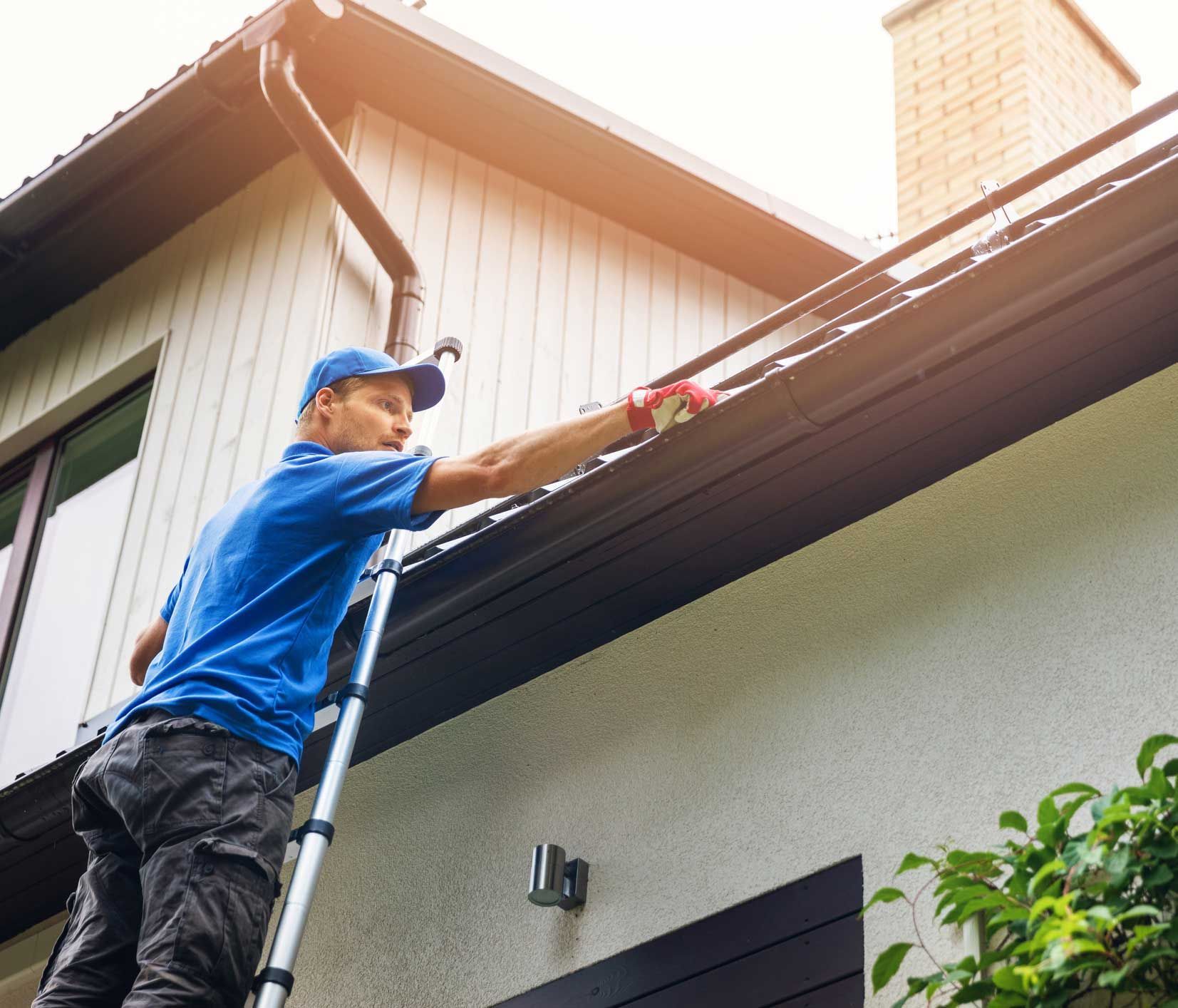 A man is standing on a ladder cleaning the gutters of a house.