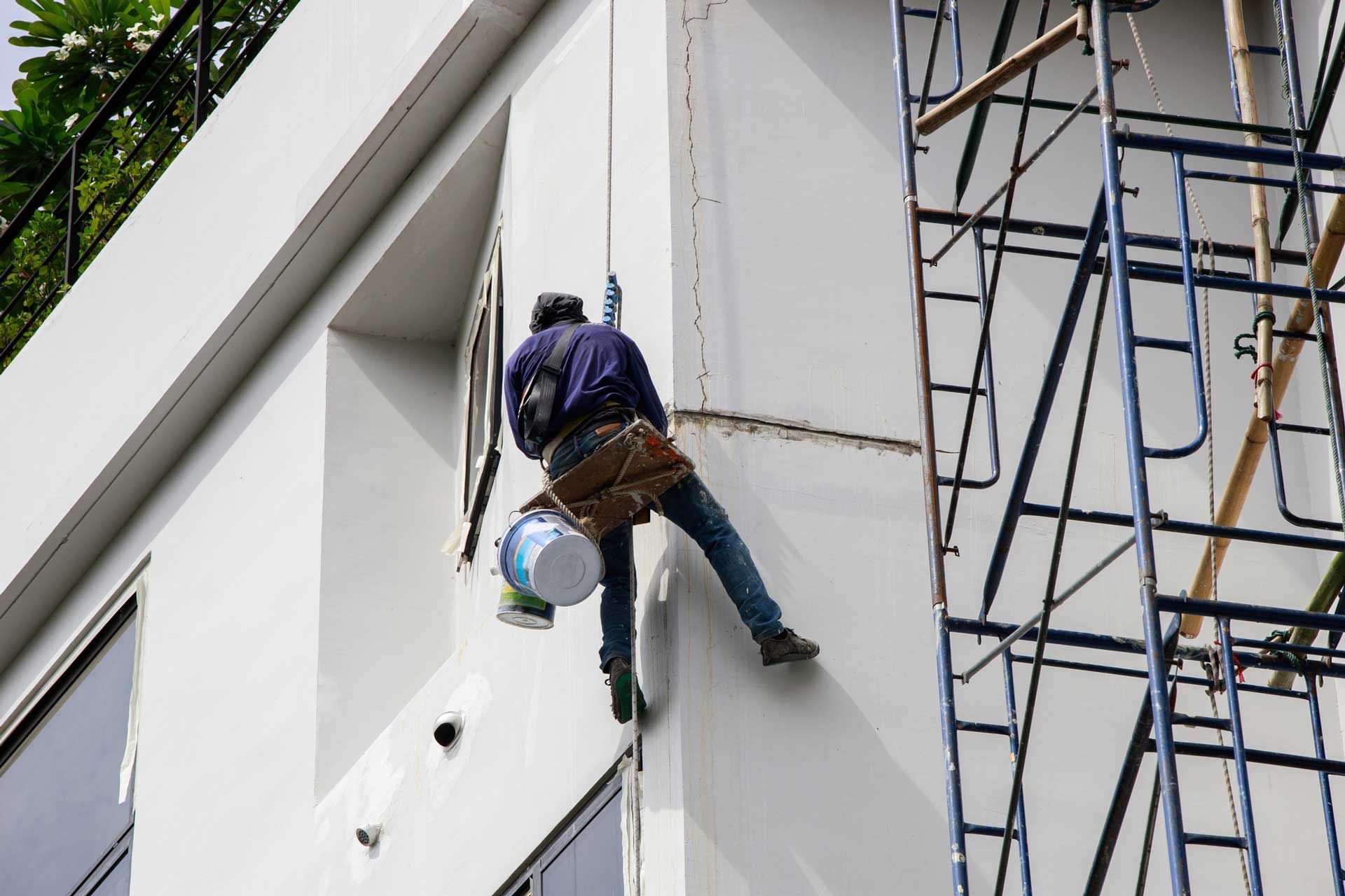 A man is climbing up a building with a bucket of paint.