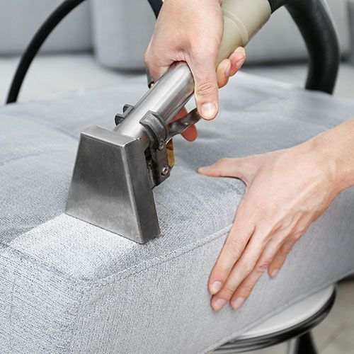 A person is cleaning a couch with a vacuum cleaner.
