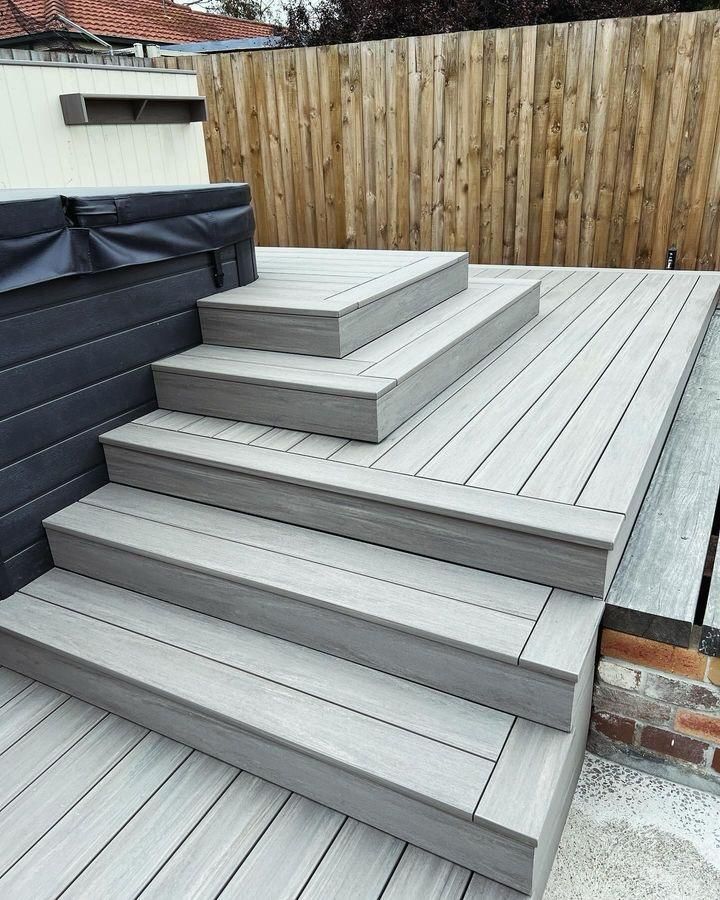 Gray composite deck with steps leading up to a hot tub, bordered by a wooden fence.