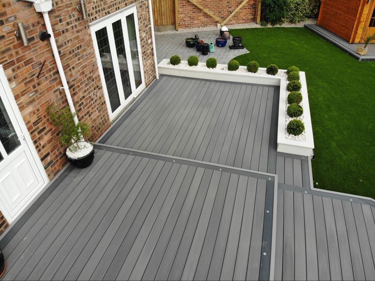 Gray composite deck with white planter boxes and green topiaries next to a brick building.
