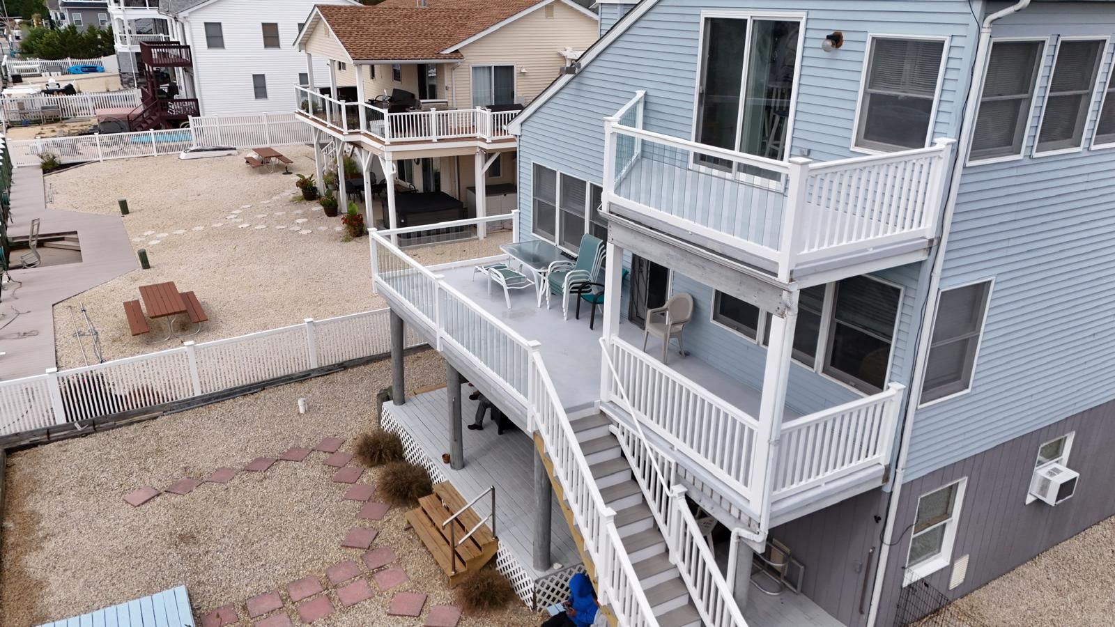 Two-story house with light blue siding, white railings, and multiple decks. Beige gravel yard.
