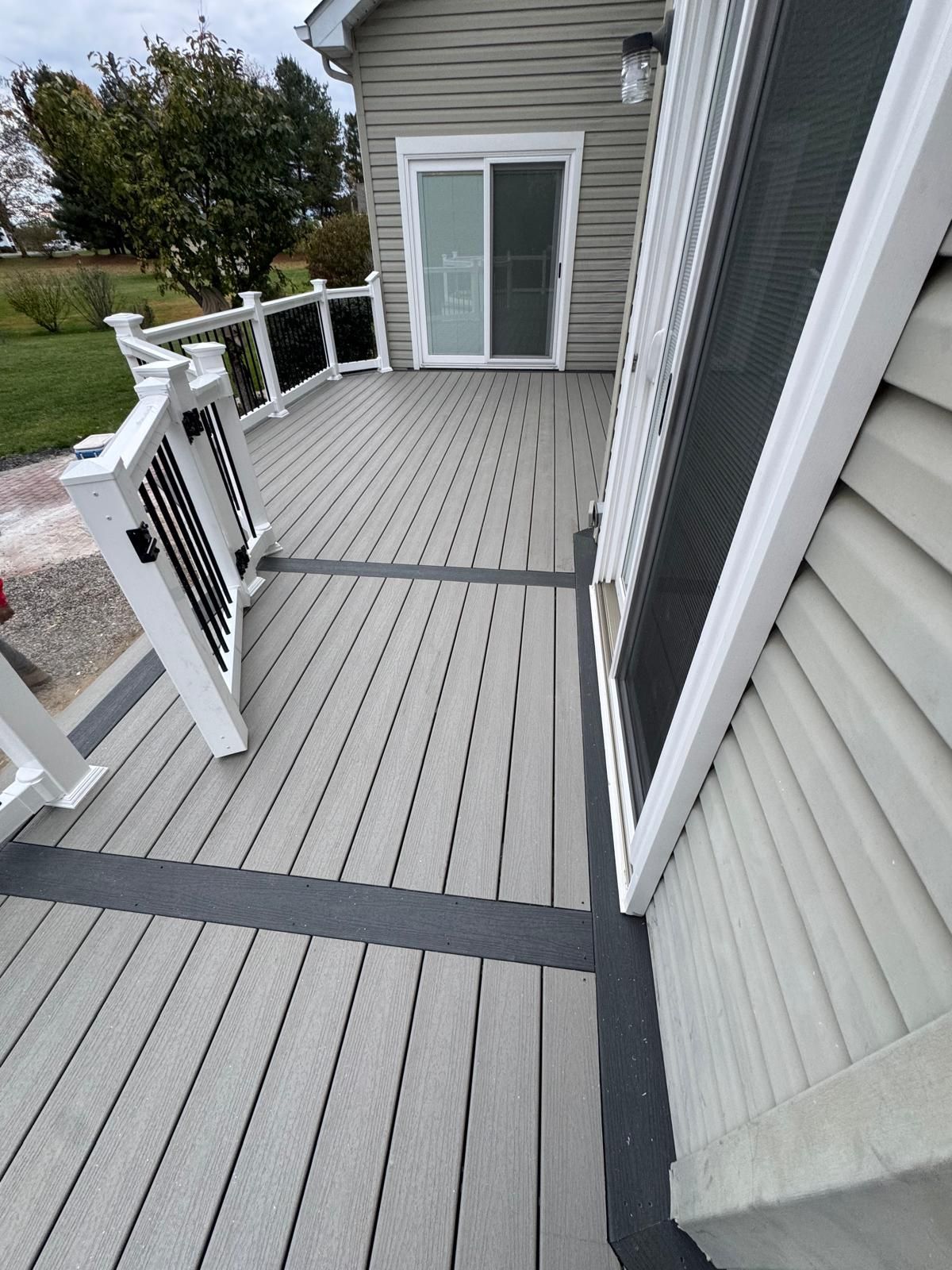 Gray composite deck with black border and white railing, leading to a sliding glass door.
