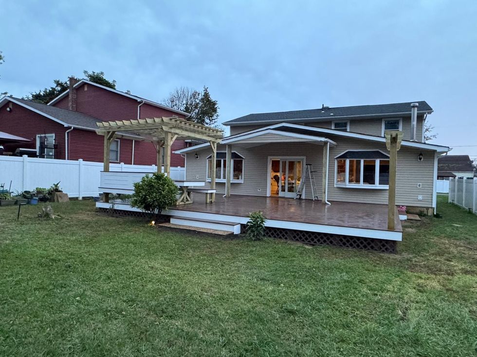 Backyard of a house with a wooden deck and pergola, green lawn, cloudy sky.