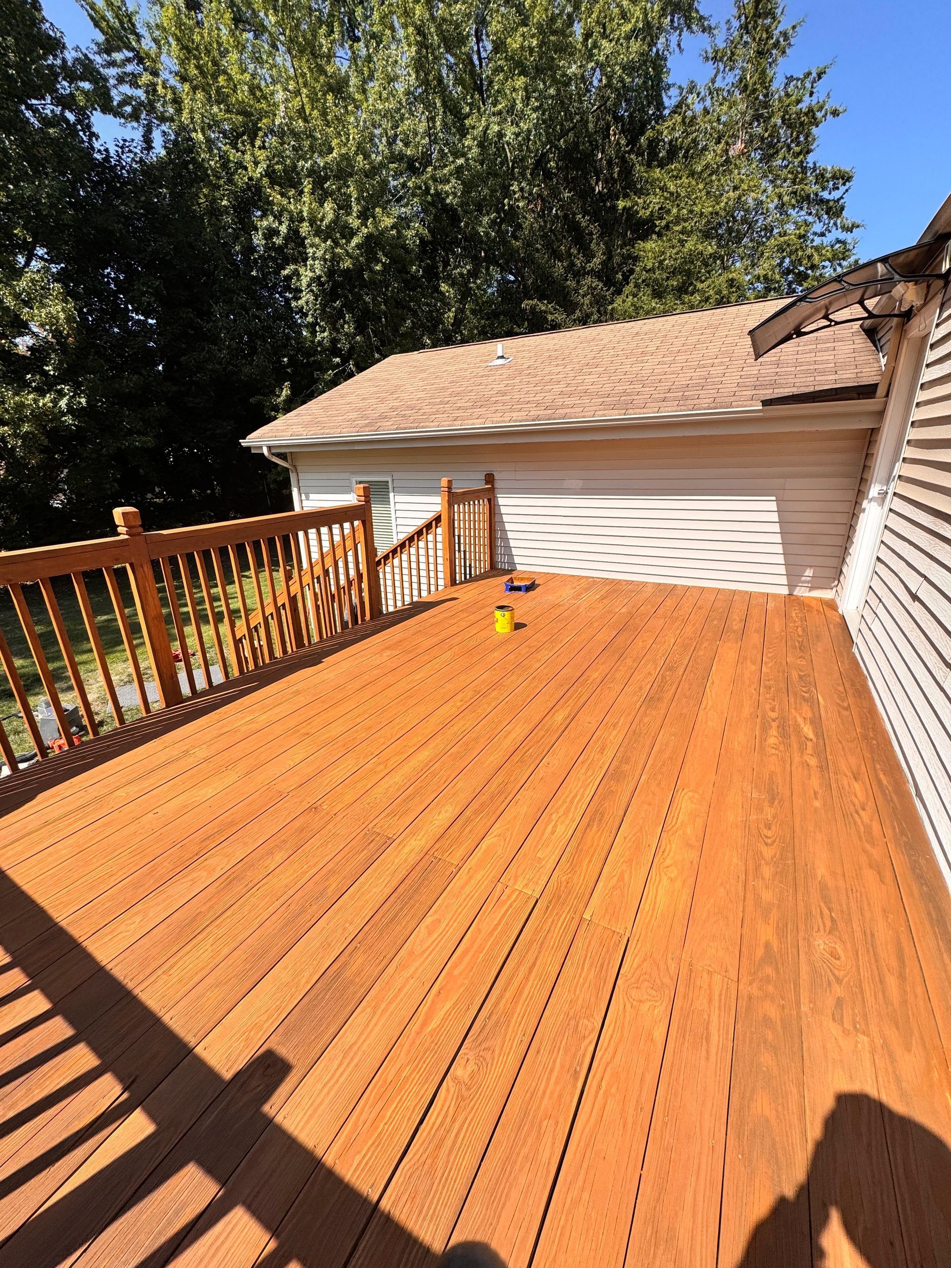 Wooden deck with brown stain, adjacent to a beige-sided building, with a wooden railing.