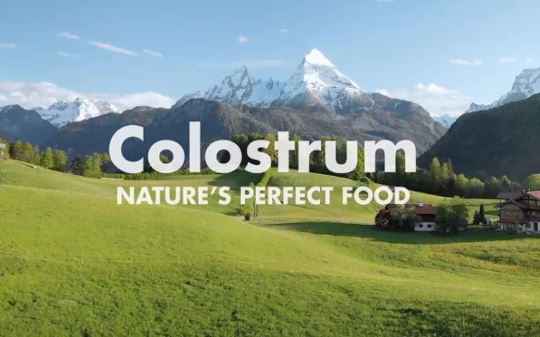A picture of a field with mountains in the background and the words colostrum nature 's perfect food.