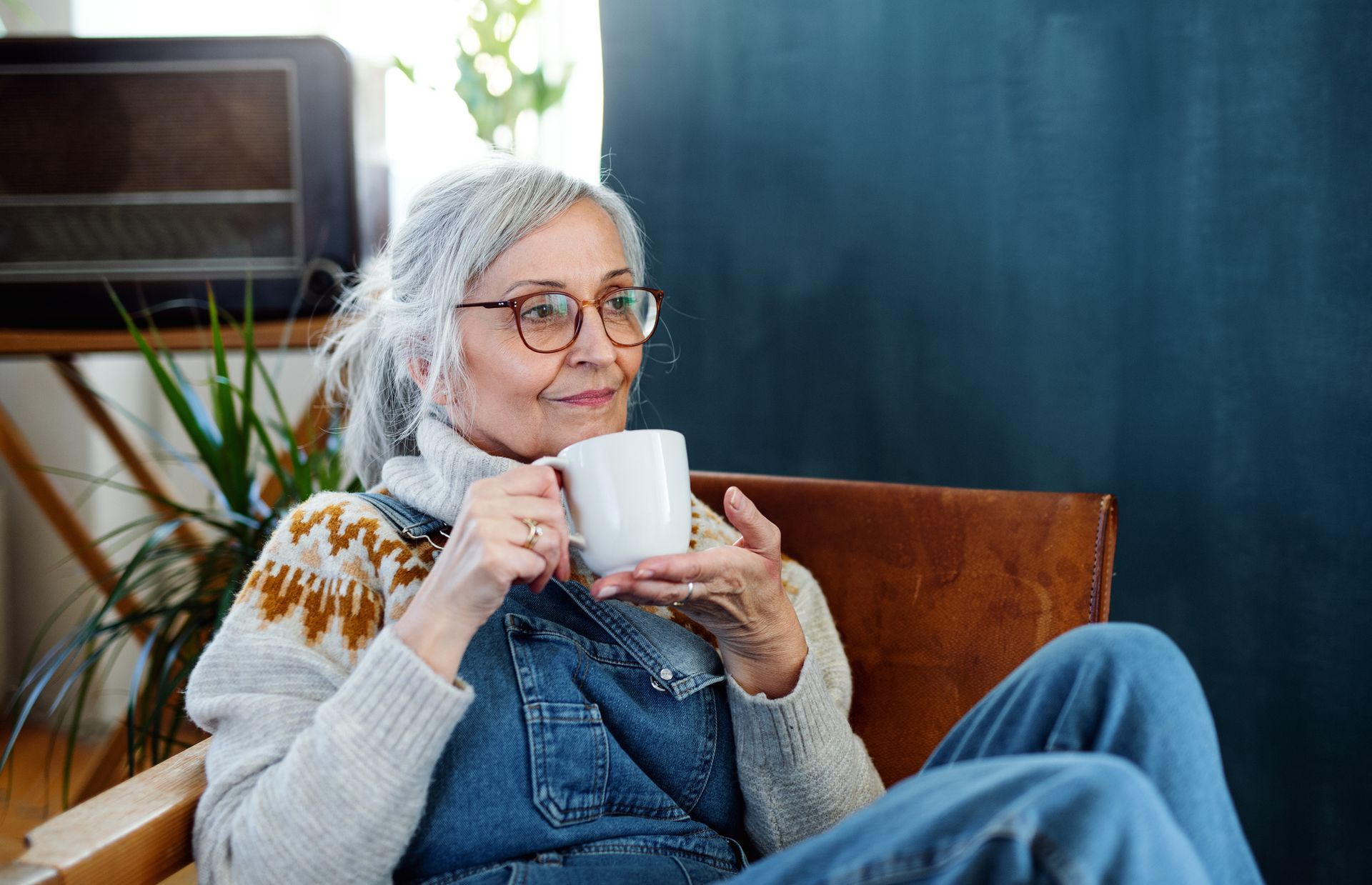 Senior woman with coffee sitting indoors in her apartment, relaxing.