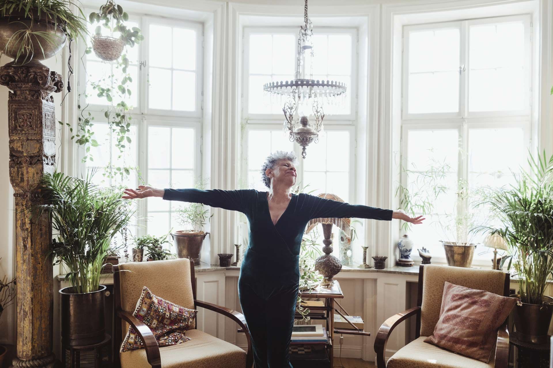 Woman enjoying sunny living room in bright senior apartments for rent with indoor plants and chairs.