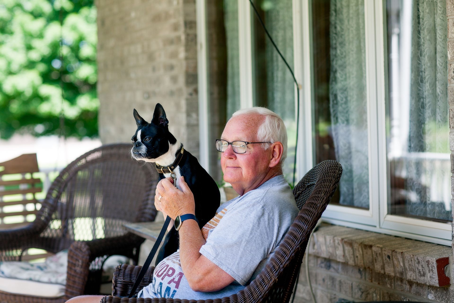 Senior man holding his Boston Terrier and sitting on the front porch of the senior housing unit.