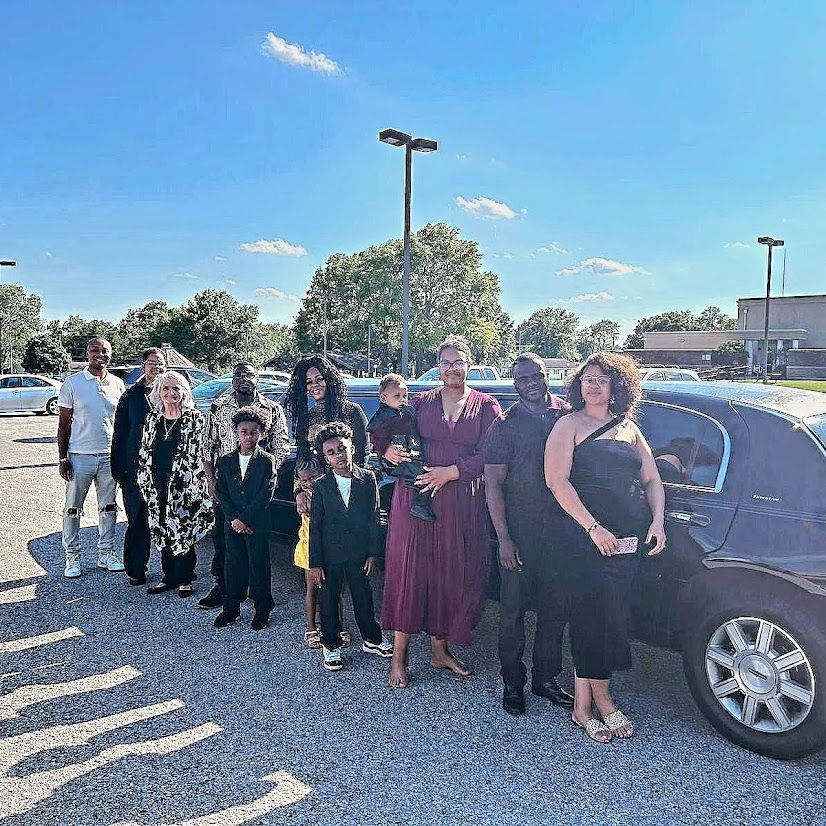 A group of people are standing in front of a limousine in a parking lot.
