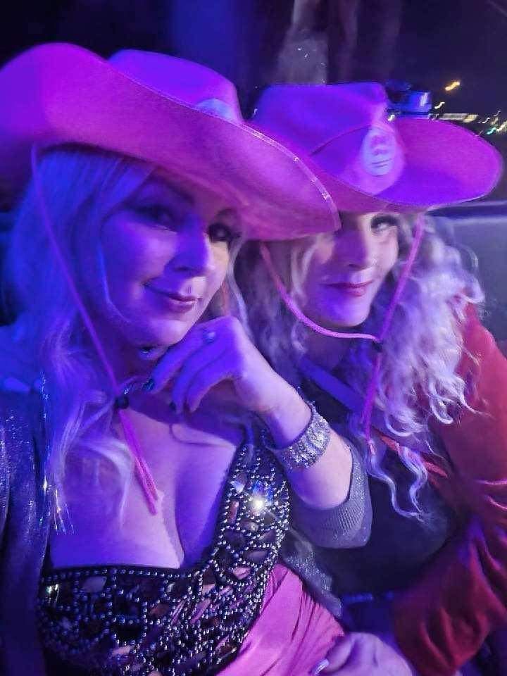 Two women wearing pink cowboy hats are sitting next to each other.