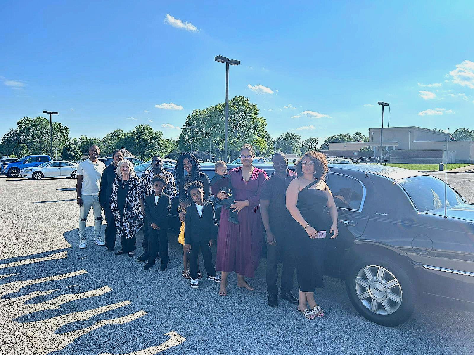 A group of people are standing in front of a limousine in a parking lot.
