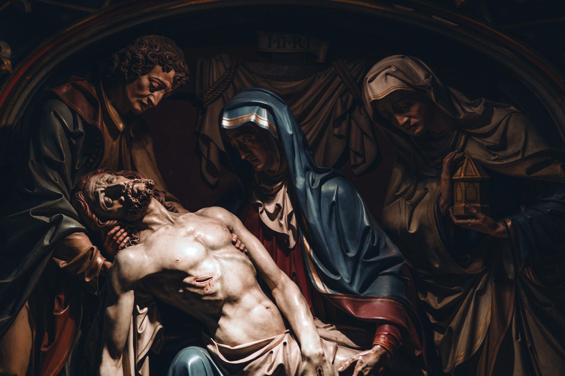 Sculpted figures of the dead Jesus held by Mary, surrounded by mourners, in a dimly lit space. SPATIAL FINE ARTS