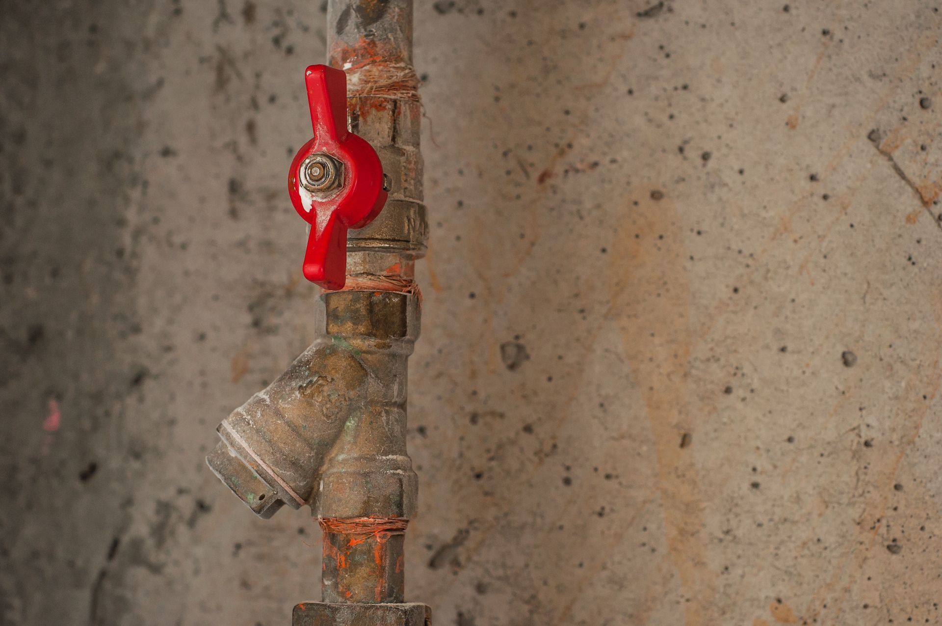 A close up of a red valve on a rusty pipe.