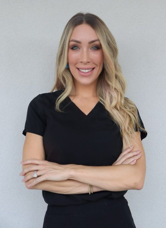 Woman in black scrubs, arms crossed, smiling.
