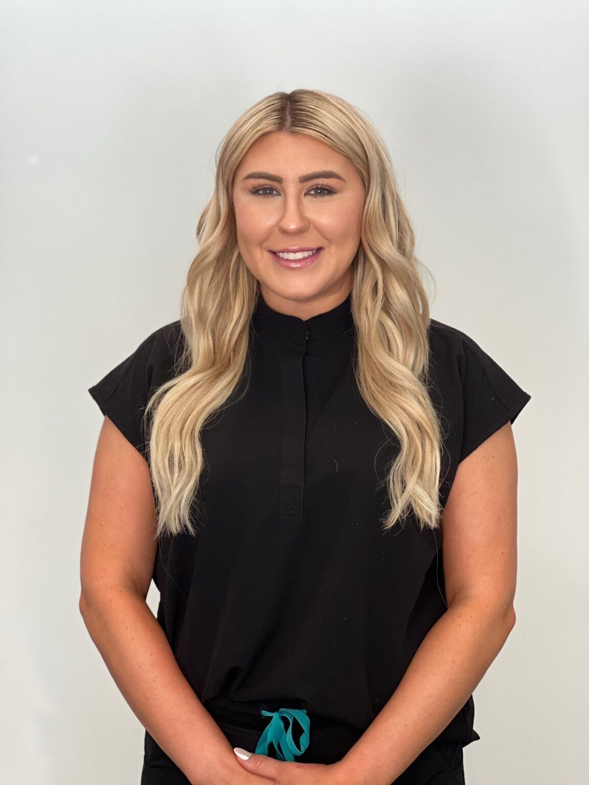 Woman with blonde wavy hair, wearing black top, smiling, against a white background.